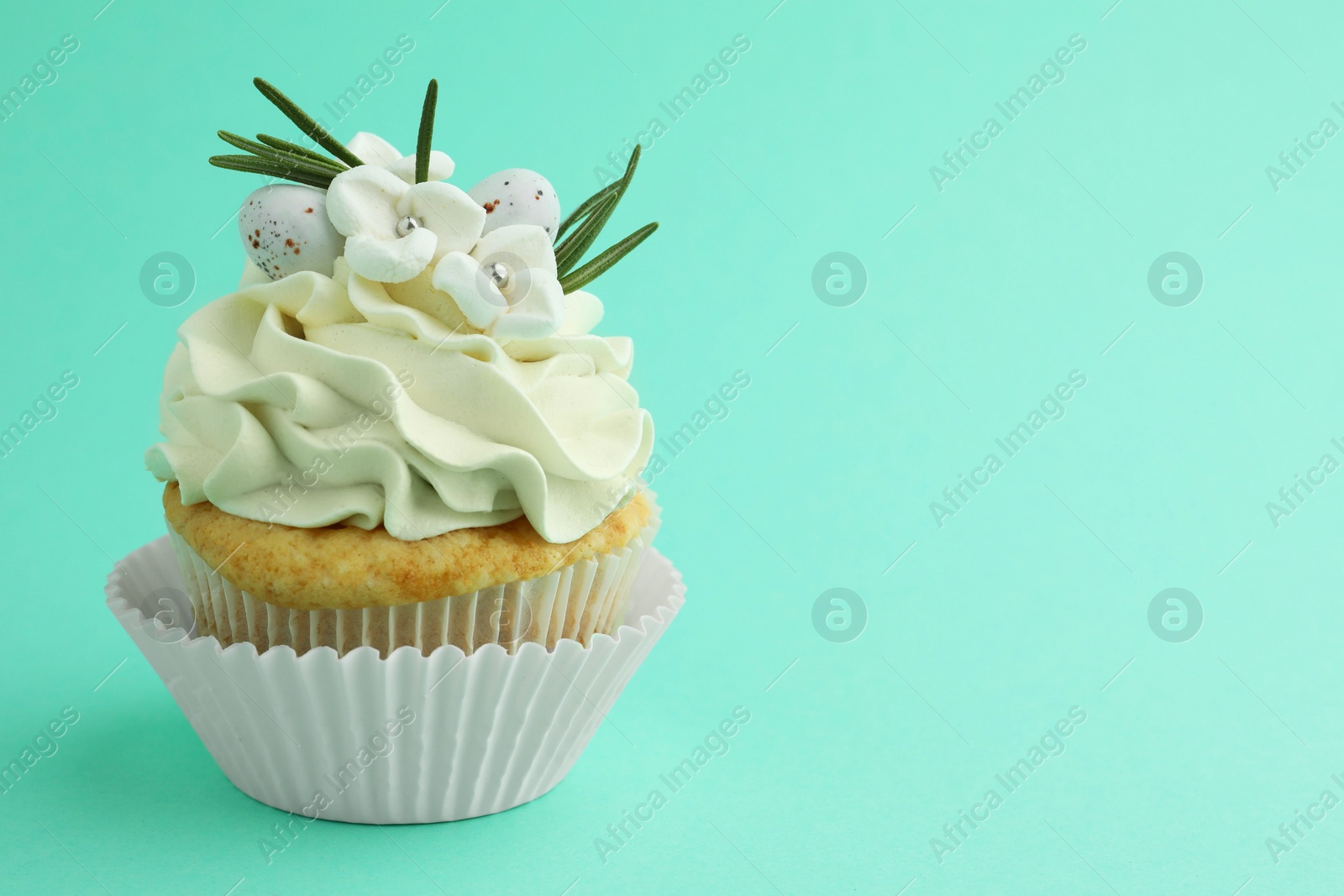 Photo of Tasty Easter cupcake with vanilla cream on turquoise background, space for text