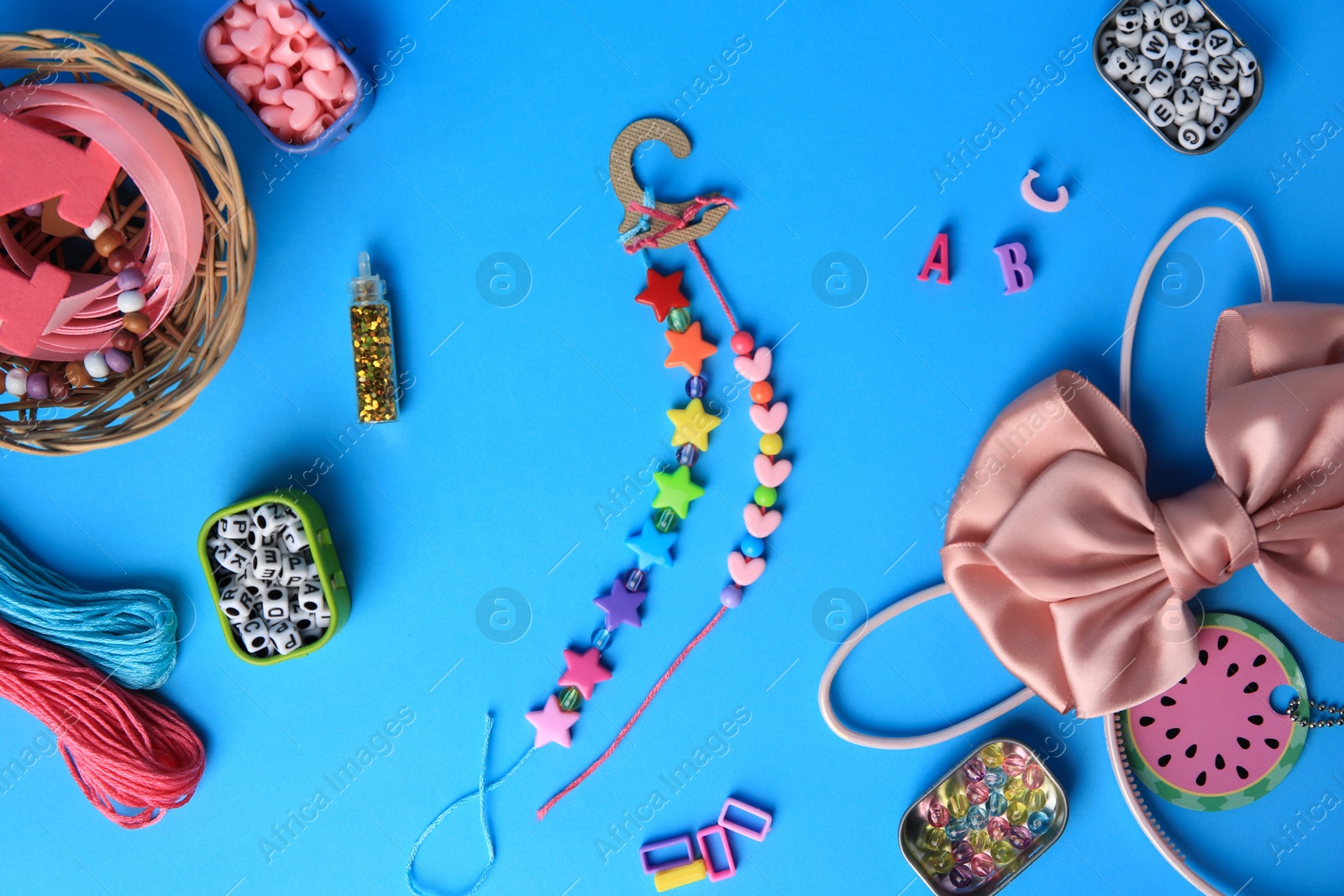 Photo of Handmade jewelry kit for kids. Colorful beads, bow, and bracelets on light blue background, flat lay