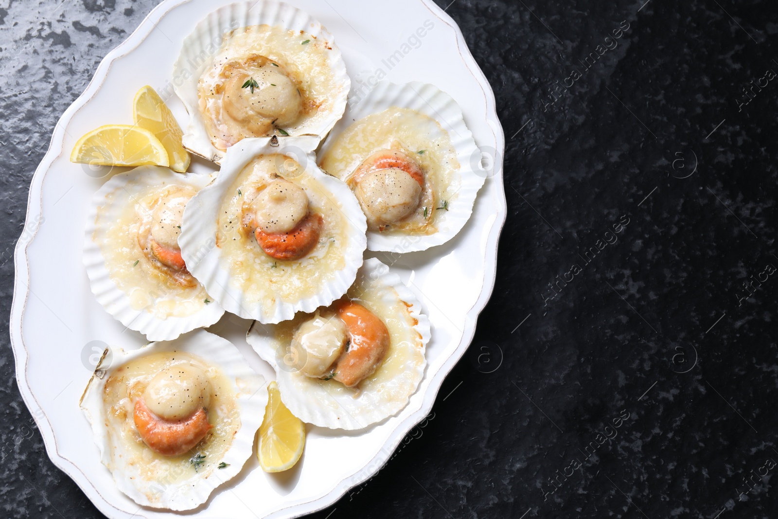 Photo of Fried scallops in shells and lemon on black textured table, top view. Space for text