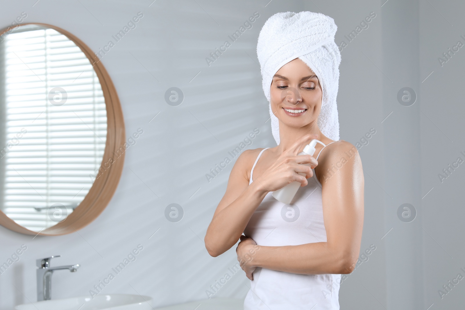 Photo of Happy woman applying body oil onto shoulder in bathroom, space for text