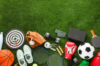 Photo of Different sport equipment and sneakers on green grass, flat lay. Space for text