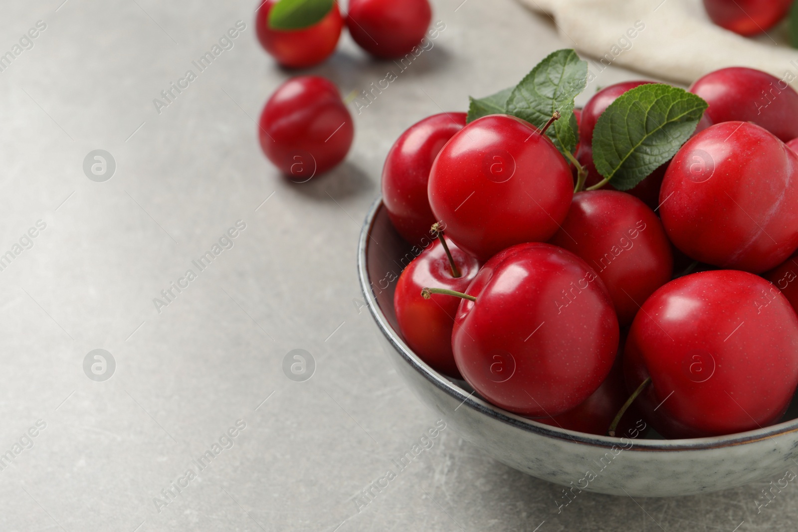 Photo of Delicious ripe cherry plums with leaves on light table. Space for text