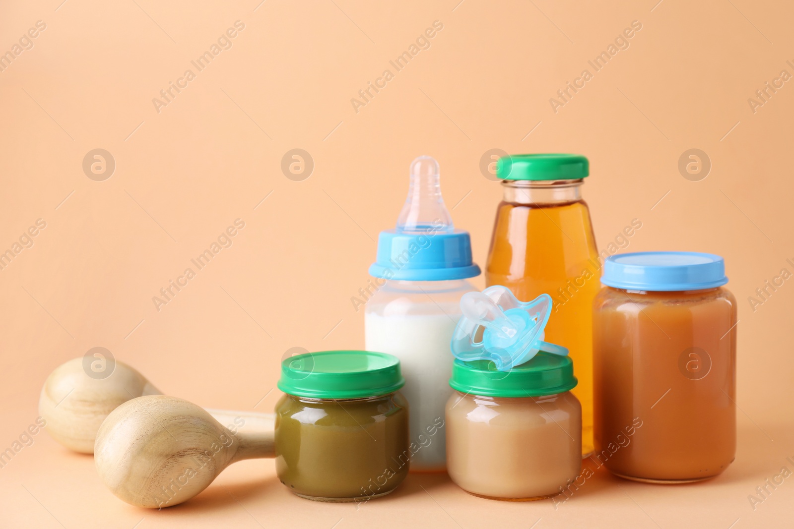 Photo of Healthy baby food, juice, milk, pacifier and toy maracas on pale orange background