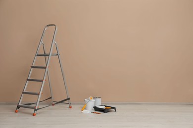 Metallic folding ladder and painting tools near beige wall indoors, space for text