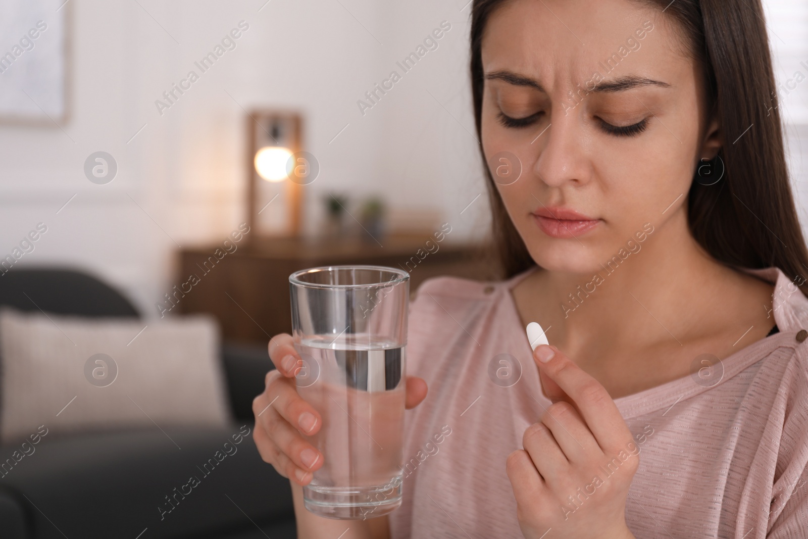 Photo of Sad young woman with abortion pill indoors