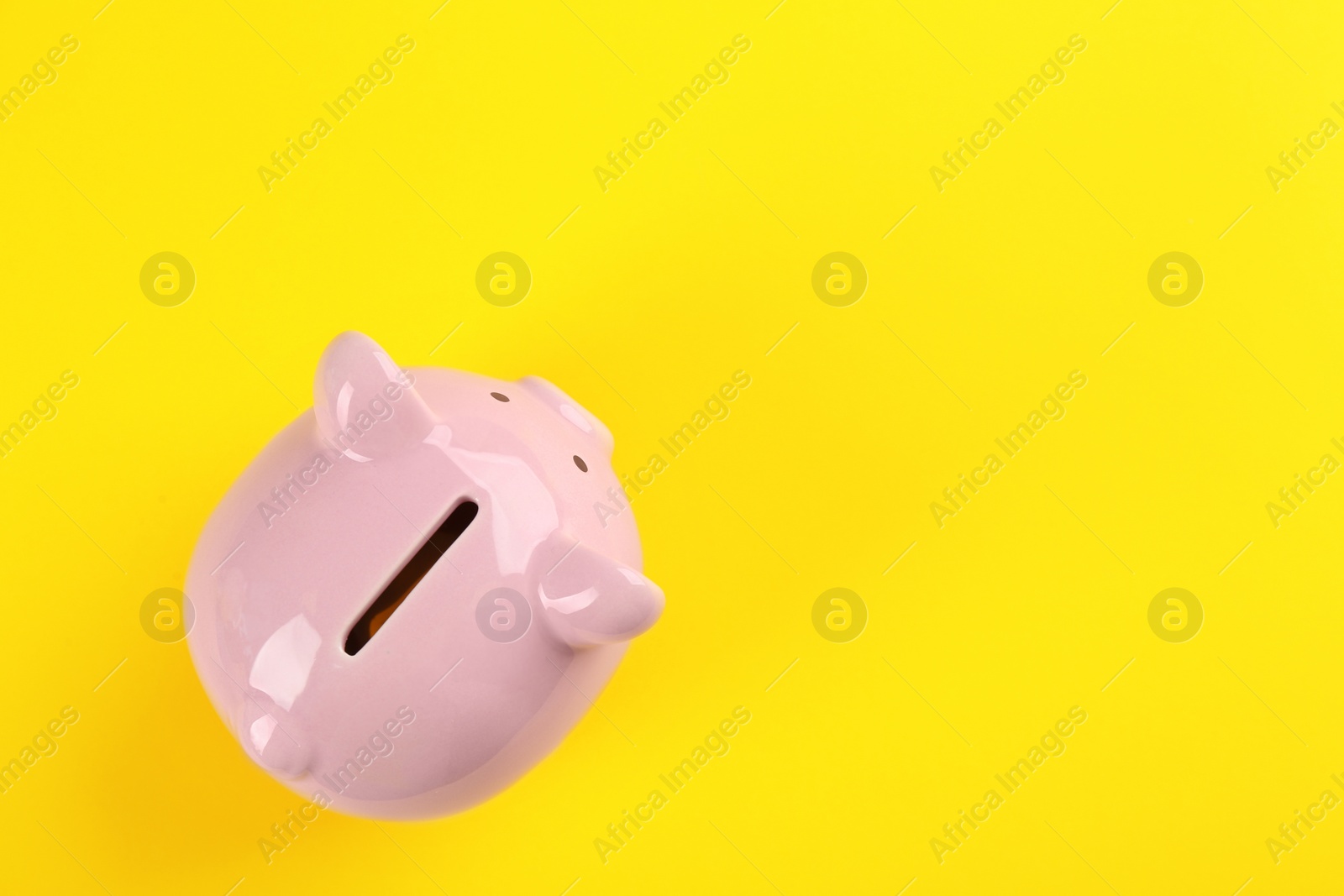 Photo of Pink piggy bank on yellow background, top view. Space for text