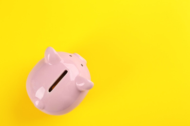 Photo of Pink piggy bank on yellow background, top view. Space for text