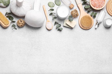 Flat lay composition with herbal massage bags, spa products and eucalyptus branches on light grey table. Space for text