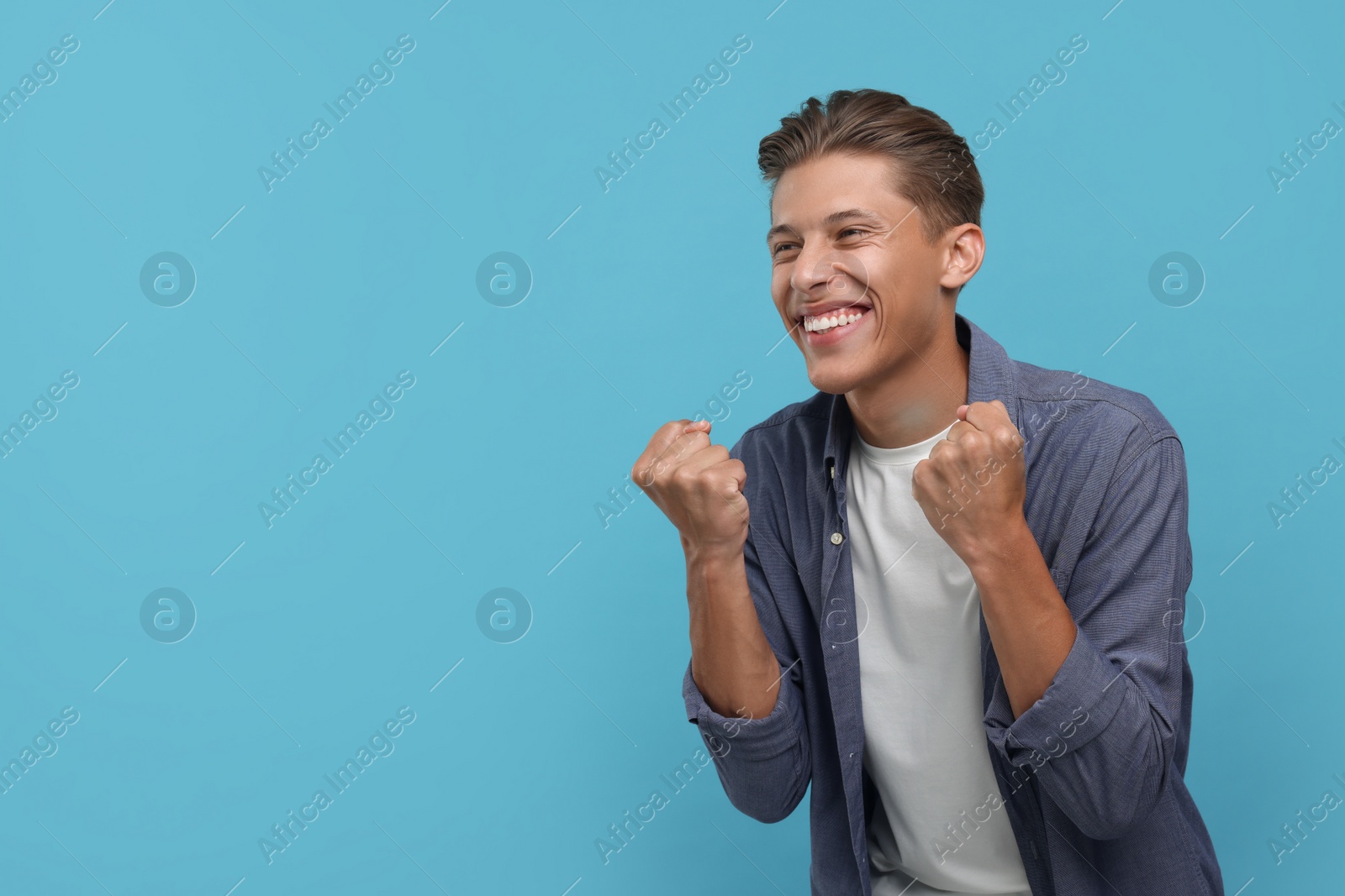 Photo of Happy sports fan celebrating on light blue background. Space for text