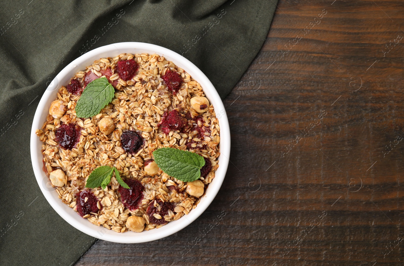 Photo of Tasty baked oatmeal with berries and nuts in bowl on wooden table, top view. Space for text