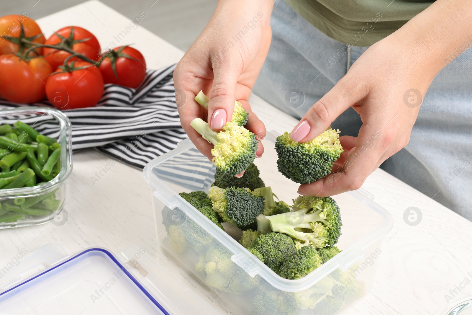 Photo of Woman putting broccoli into plastic container at white wooden table, closeup. Food storage