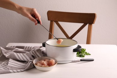 Photo of Woman dipping piece of raw meat into oil in fondue pot at white wooden table, closeup