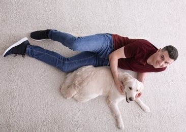 Photo of Handsome man with dog lying on carpet at home