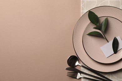 Photo of Stylish table setting. Plates, cutlery, blank card and green twig on beige background, top view with space for text