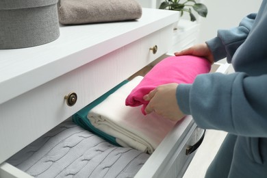 Woman putting folded clothes into drawer indoors, closeup