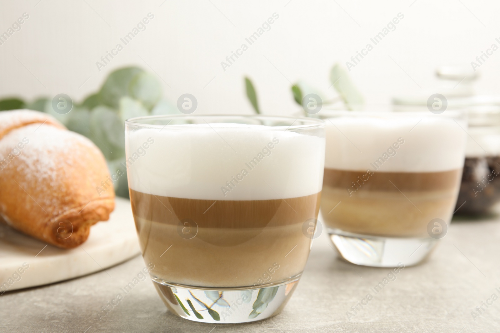 Photo of Delicious latte macchiato and croissant on light grey table