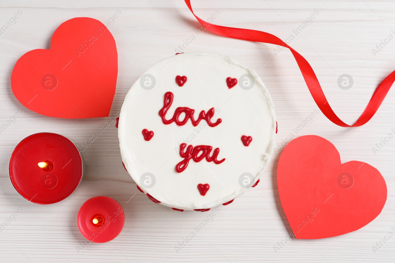 Photo of Bento cake with text Love You, candles and paper hearts on white wooden table, flat lay. St. Valentine's day surprise