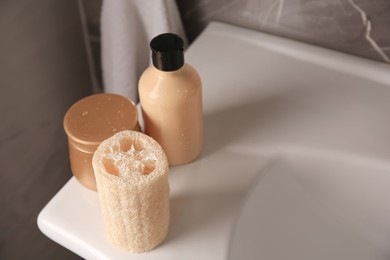 Natural loofah sponge and cosmetic products on washbasin in bathroom. Space for text
