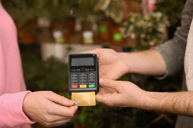 Photo of Woman using credit card for terminal payment in floral shop, closeup