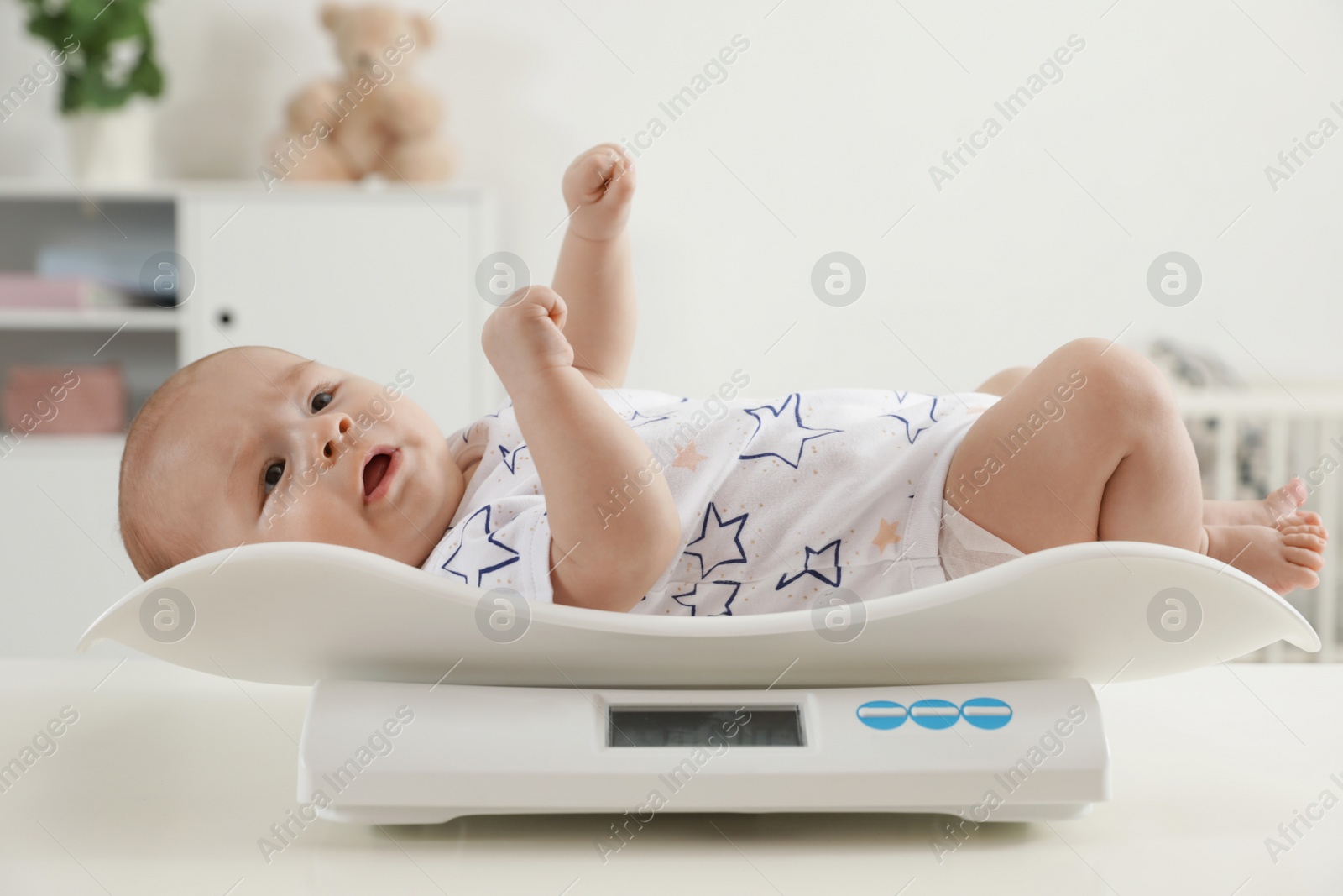 Photo of Cute little baby lying on scales in light room