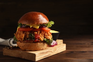 Photo of Delicious burger with crispy chicken patty on wooden table. Space for text