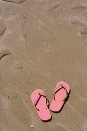 Photo of Stylish pink flip flops on wet sand, above view. Space for text