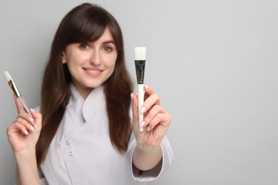 Photo of Cosmetologist with cosmetic brushes on grey background, selective focus. Space for text