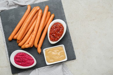 Photo of Delicious sausages, ketchup, mustard and horseradish on grey table, flat lay. Space for text