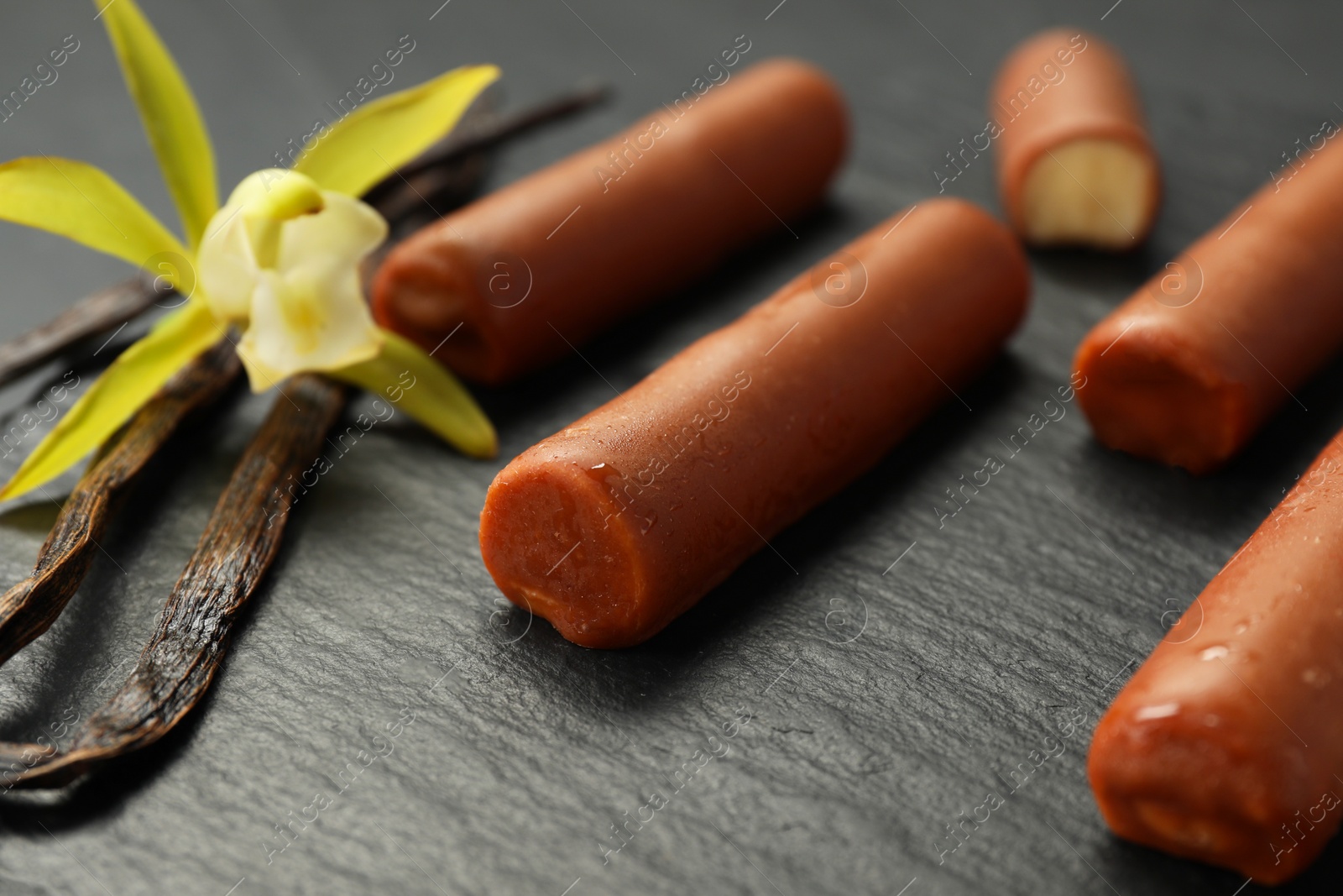 Photo of Glazed curd cheese bars, vanilla pods and flower on black table, closeup