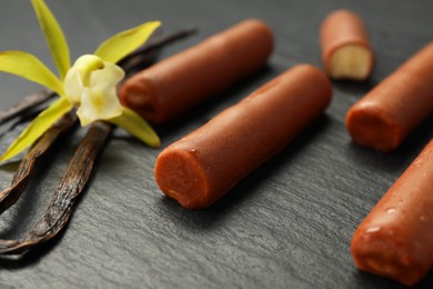 Photo of Glazed curd cheese bars, vanilla pods and flower on black table, closeup