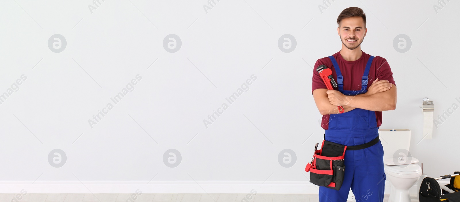 Image of Young man with plumber wrench near toilet bowl indoors, space for text. Banner design