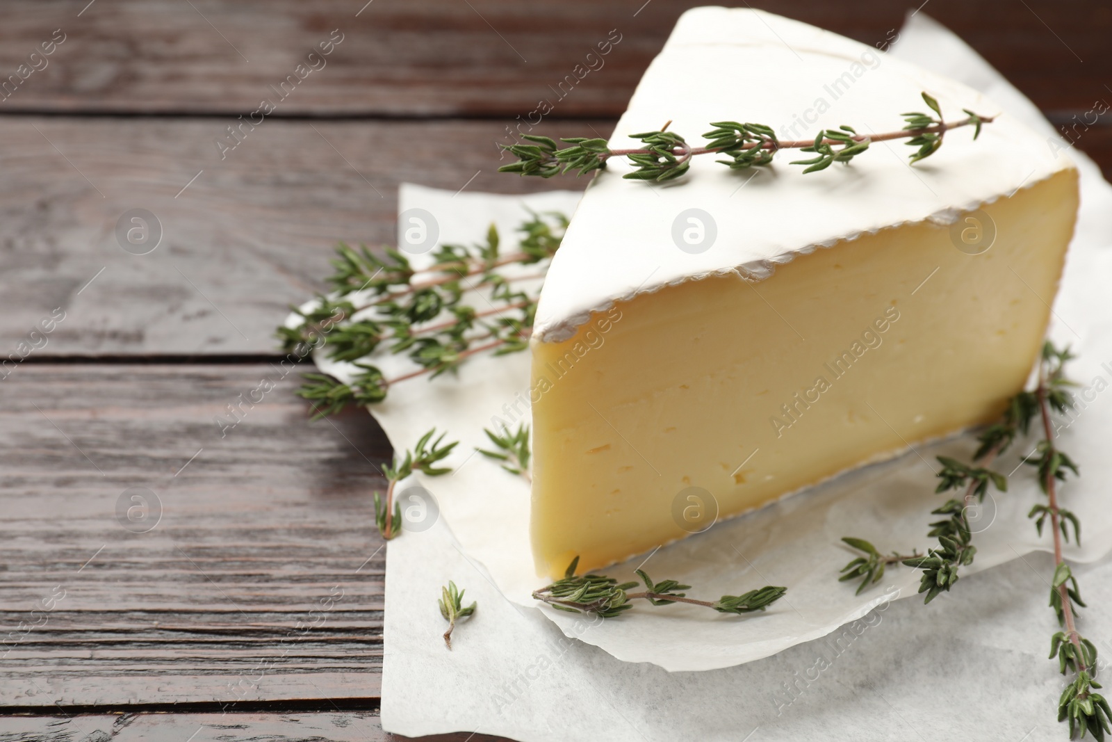 Photo of Piece of tasty camembert cheese and thyme on wooden table, closeup. Space for text