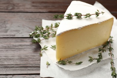 Piece of tasty camembert cheese and thyme on wooden table, closeup. Space for text