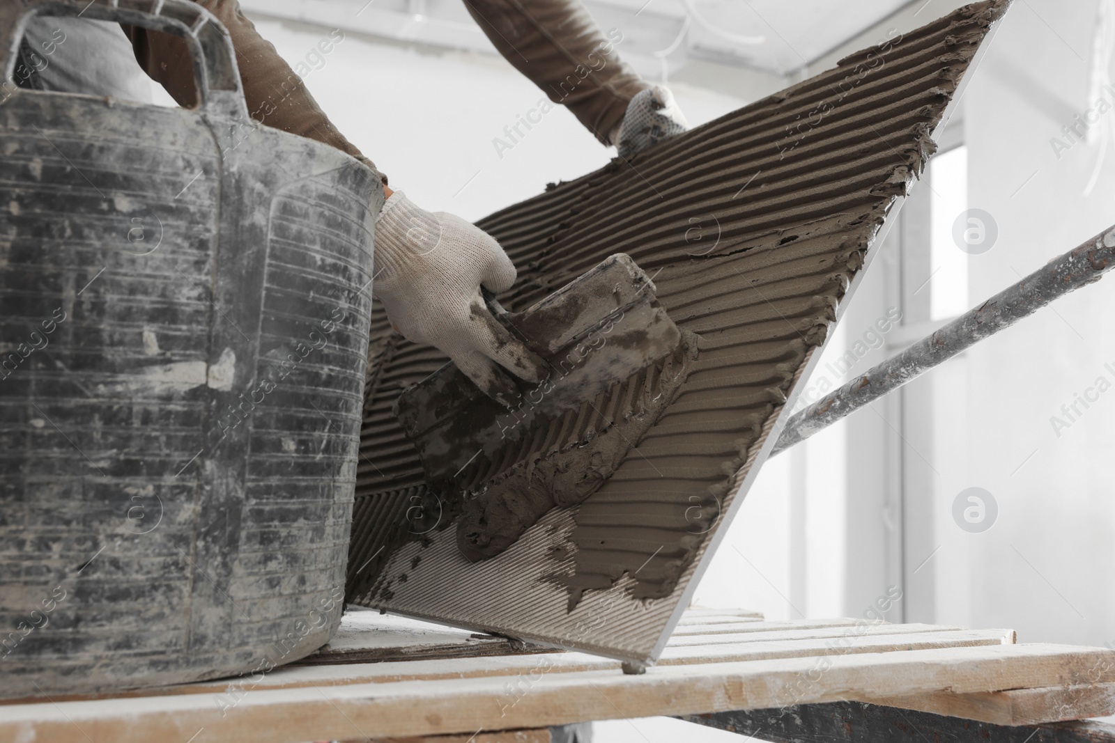 Photo of Worker applying cement on tile for installation in room, closeup