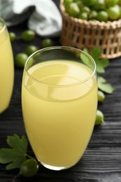 Photo of Tasty gooseberry juice in glass on black wooden table, closeup