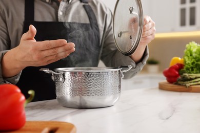 Photo of Man with pot smelling dish after cooking at white marble countertop in kitchen, closeup