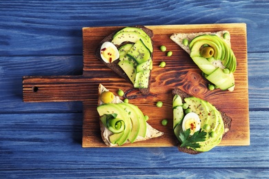 Tasty crisp toasts with avocado on wooden board, top view