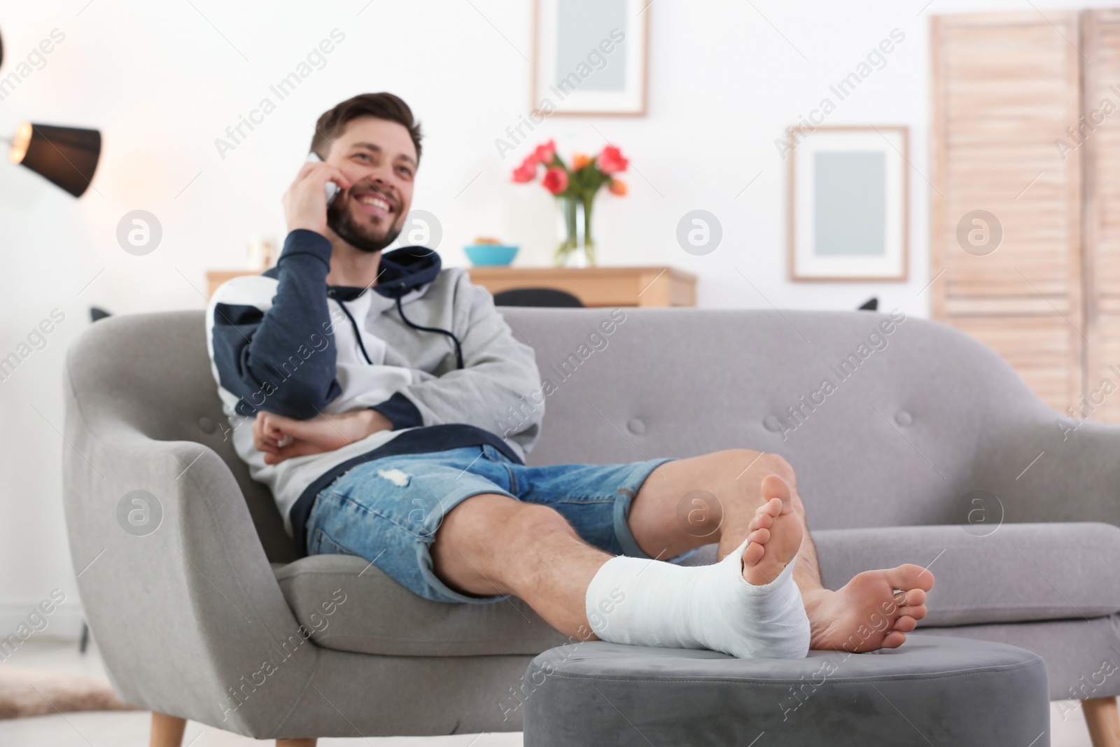 Photo of Man with broken leg in cast using mobile phone while sitting on sofa at home