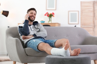 Man with broken leg in cast using mobile phone while sitting on sofa at home