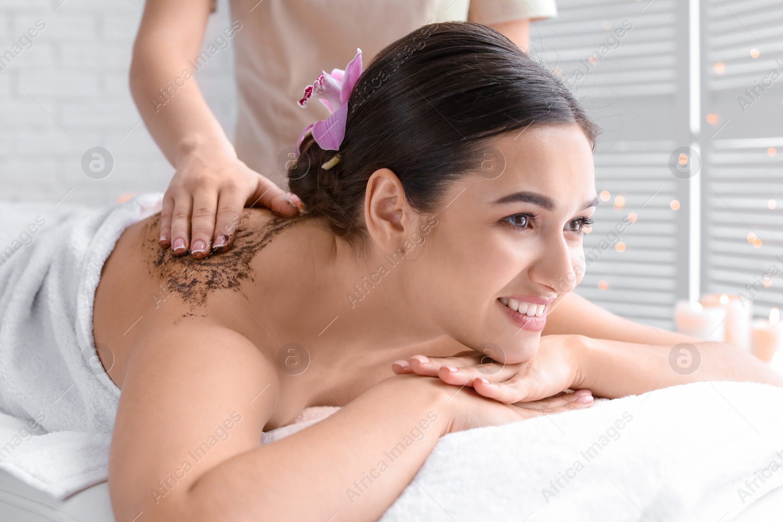 Photo of Young woman having body scrubbing procedure in spa salon