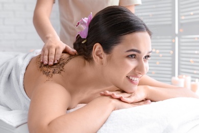 Young woman having body scrubbing procedure in spa salon