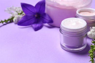 Jars of body cream and flowers on lilac background. Space for text