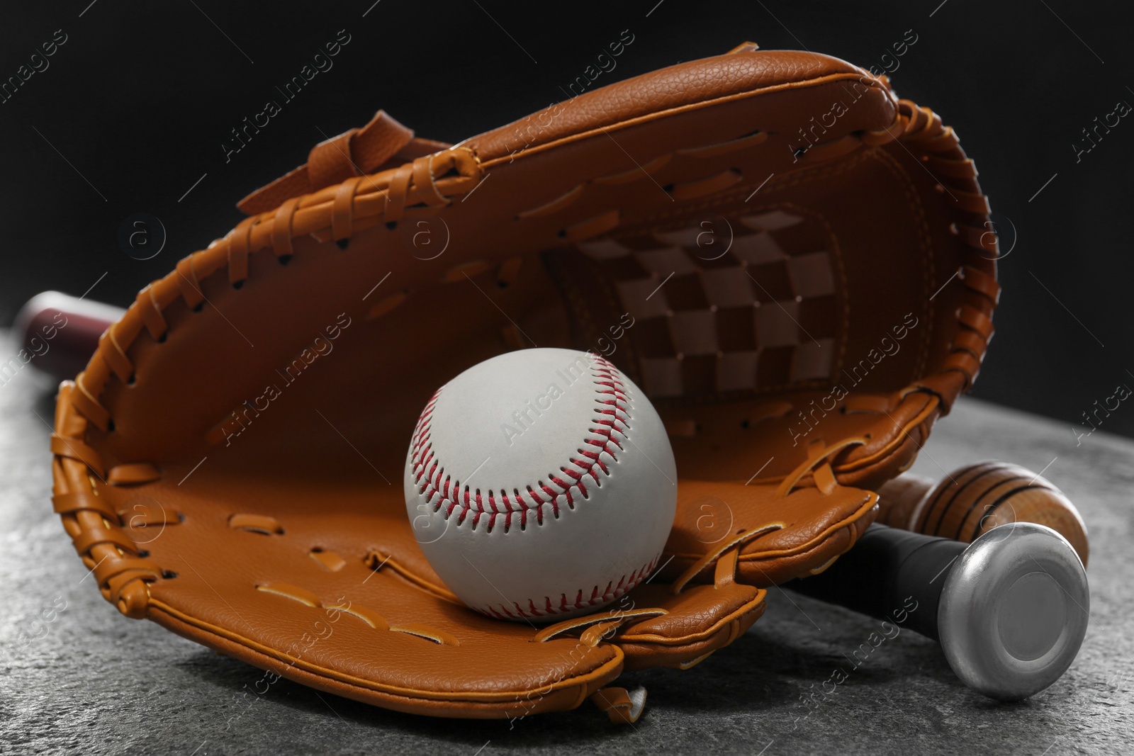 Photo of Baseball bats, glove and ball on grey table, closeup