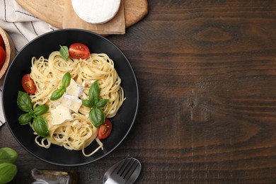 Delicious pasta with brie cheese, tomatoes and basil leaves served on wooden table, flat lay. Space for text