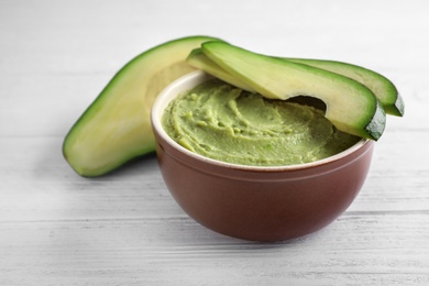 Photo of Bowl with guacamole sauce and ripe avocados on white wooden table