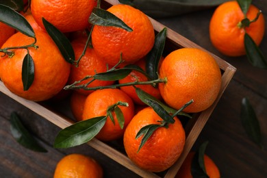 Photo of Fresh ripe tangerines with green leaves in crate on wooden table, flat lay