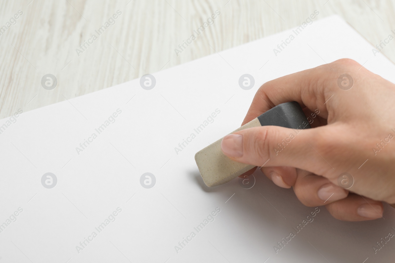 Photo of Woman erasing something in notebook at white wooden table, closeup