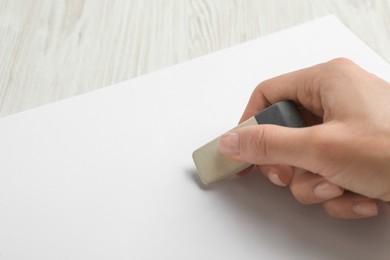 Photo of Woman erasing something in notebook at white wooden table, closeup