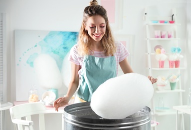 Young woman making cotton candy using modern machine in room