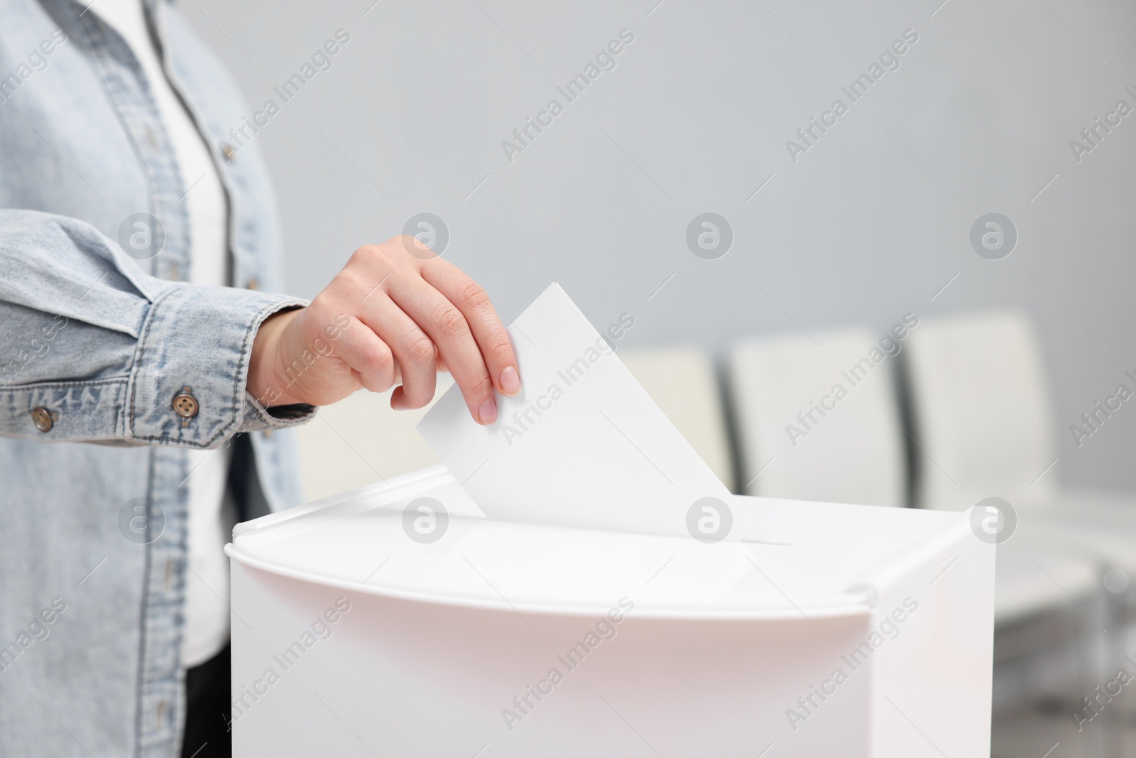 Photo of Woman putting her vote into ballot box on blurred background, closeup